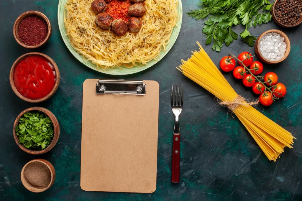 Pasta, tomatoes and spices beside a blank clipboard on a kitchen prep counter, showing the station detail an F&B SOP consultant documents