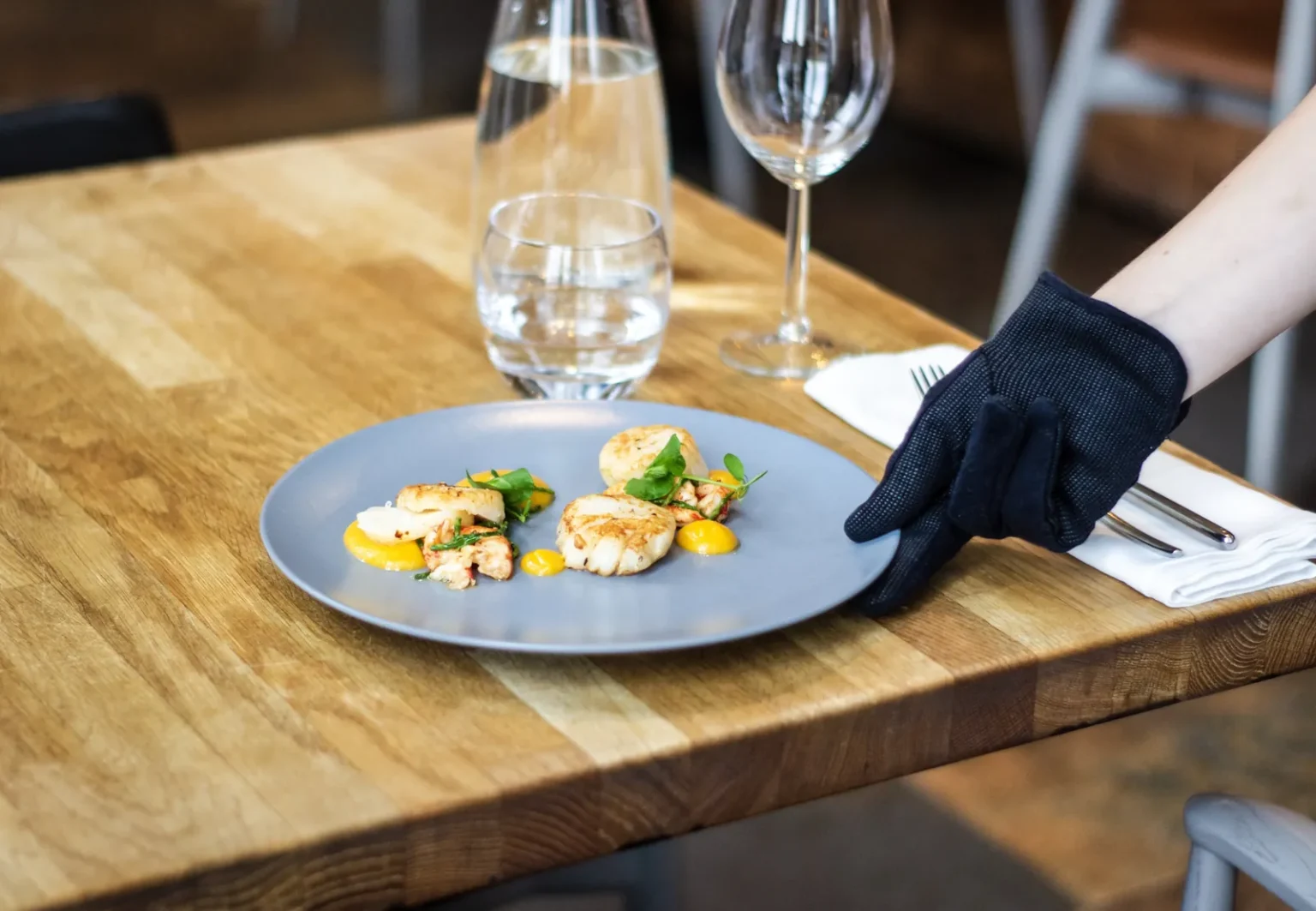 American service: a gloved server places a plated dish of seared scallops on a restaurant table