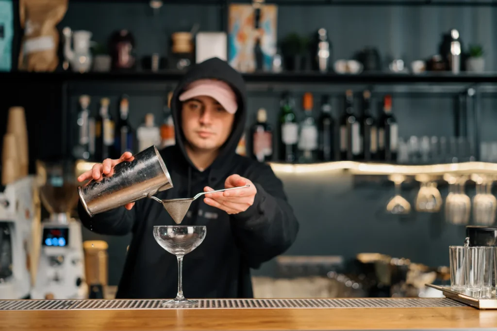 Bartender course fees: bartender preparing a cocktail at a bar in the evening