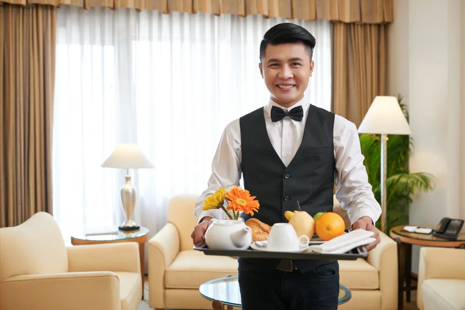 Butler service in a hotel suite: a butler in a waistcoat and bow tie carries a breakfast tray