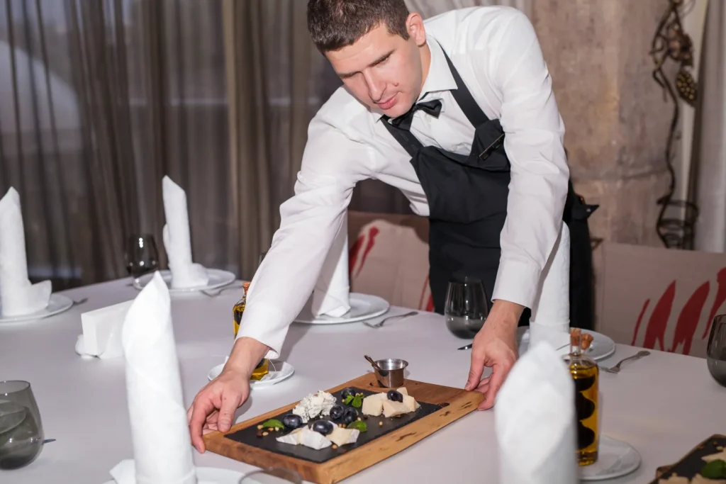 Gueridon service: a waiter arranges a gourmet cheese platter at an elegant table