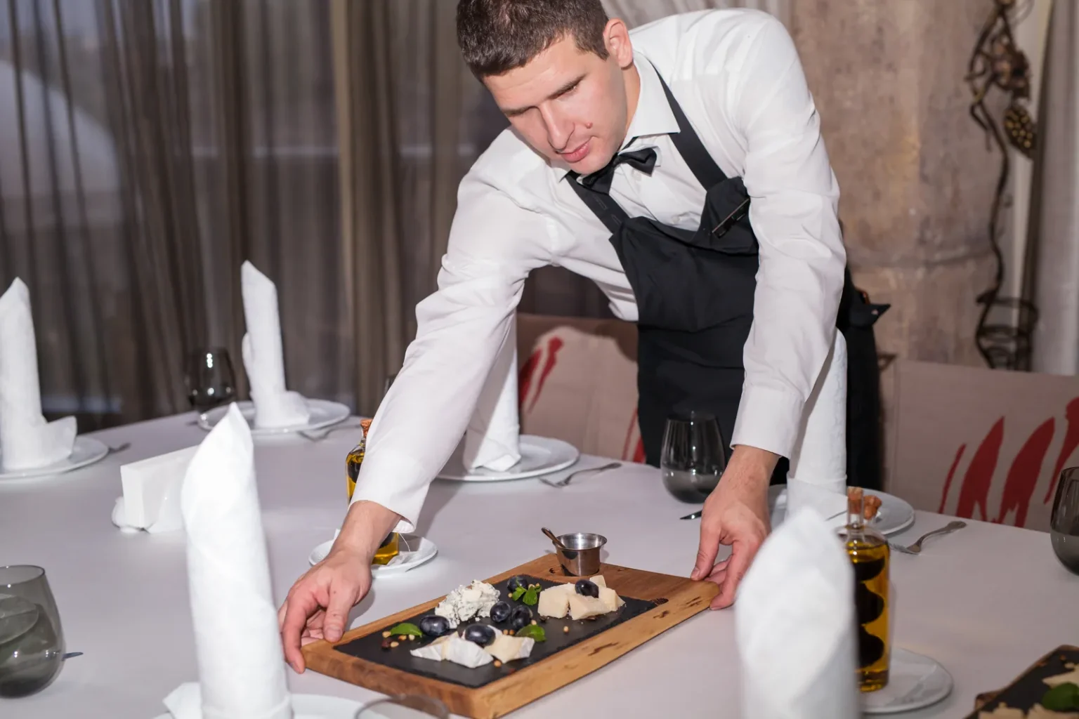 Gueridon service: a waiter arranges a gourmet cheese platter at an elegant table