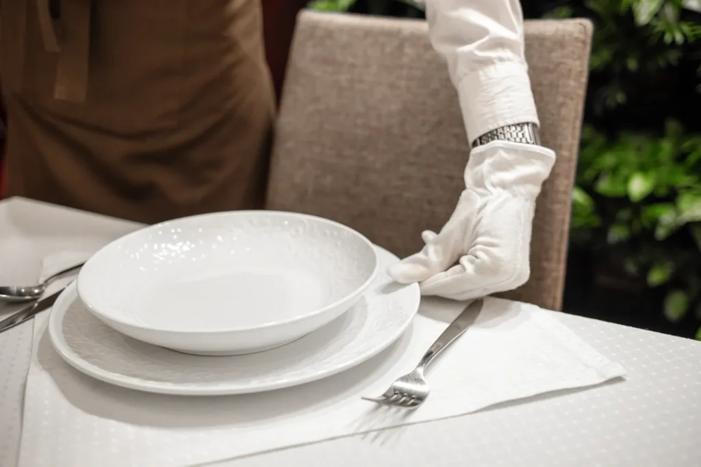 Silver service: a server in white gloves sets a fine dining table for a formal dinner