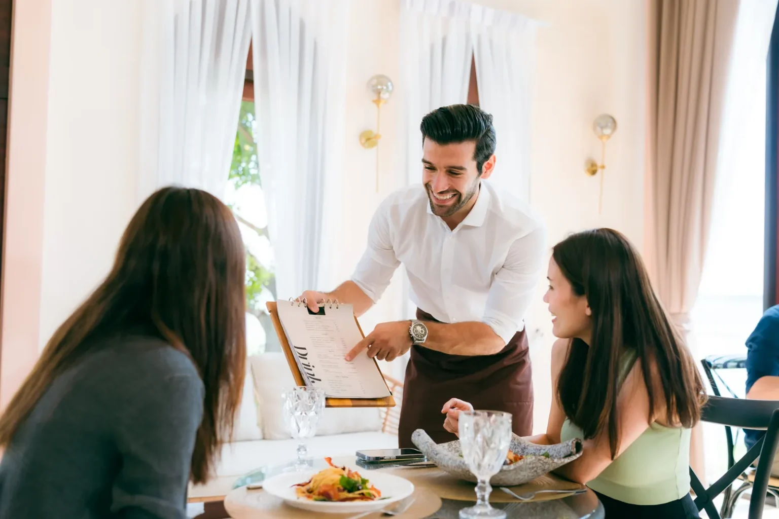 Server explaining the menu to two diners, one of the types of restaurant service in a table-service restaurant